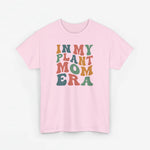 Roze T-shirt met ronde hals en multikleurenprint “IN MY PLANT MOM ERA” (voorzijde).