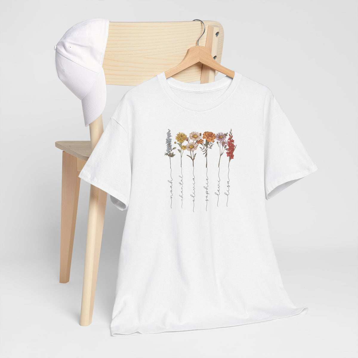 Wit T-shirt met bloemenrij en namenprint, opgevouwen op een stoel