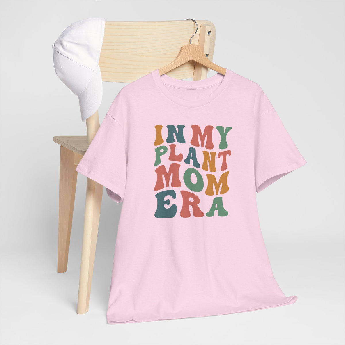 Roze T-shirt aan hanger, ronde hals en multikleurenprint “IN MY PLANT MOM ERA”.
