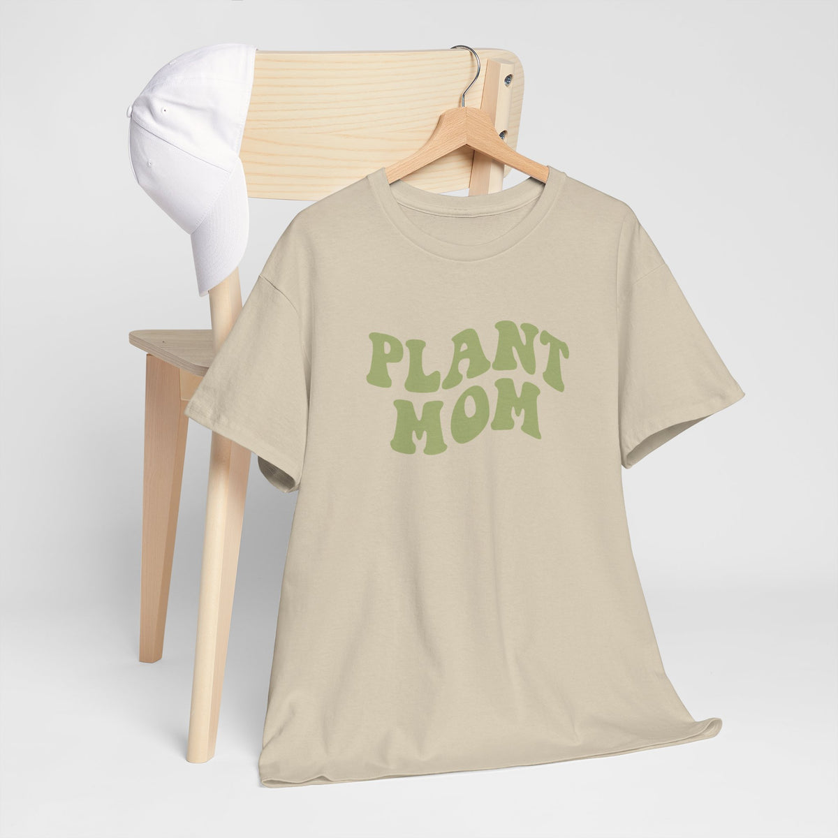 Beige T-shirt aan hanger met groene “PLANT MOM” tekst, korte mouwen.
