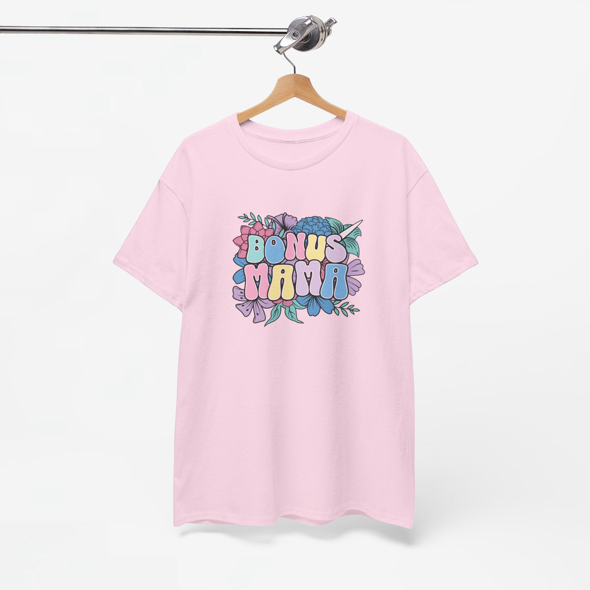 Roze T-shirt met bloemenprint en kleurrijke tekst “BONUS MAMA”, aan een houten hanger.