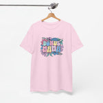 Roze T-shirt met bloemenprint en kleurrijke tekst “BONUS MAMA”, aan een houten hanger.
