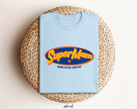 Lichtblauwe T-shirt met ronde hals en SuperMam-logo op de borst, op gevlochten mand