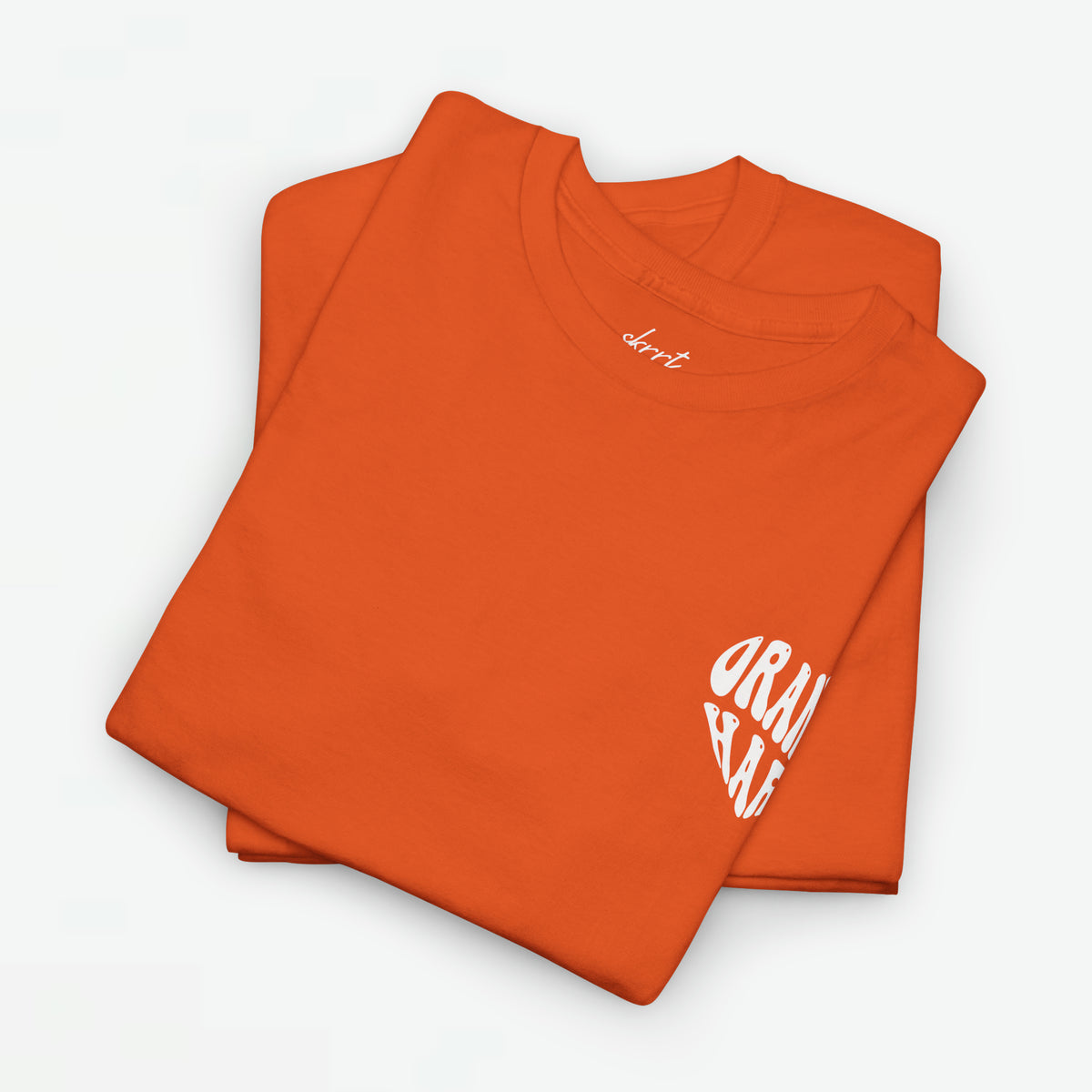 Oversized Koningsdag T-shirt voor dames, oranje stof met klein wit borstlogo, opgevouwen.