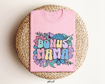 Roze oversized t-shirt met grote bloemenprint en tekst 'BONUS MAMA'.