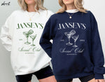 Twee sweatshirts: witte en navy, beide met JANSEN'S Social Club opdruk.