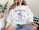 Witte sweatshirt met ronde hals en blauwe 'JANSEN'S Social Club'-opdruk, gedragen.