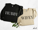 Koppeltruienset: zwarte 'HUBBY' en beige 'WIFEY' sweater.