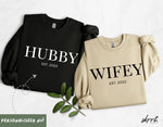 Twee truien: zwarte met “HUBBY” en beige met “WIFEY”, beide met “EST. 2022”