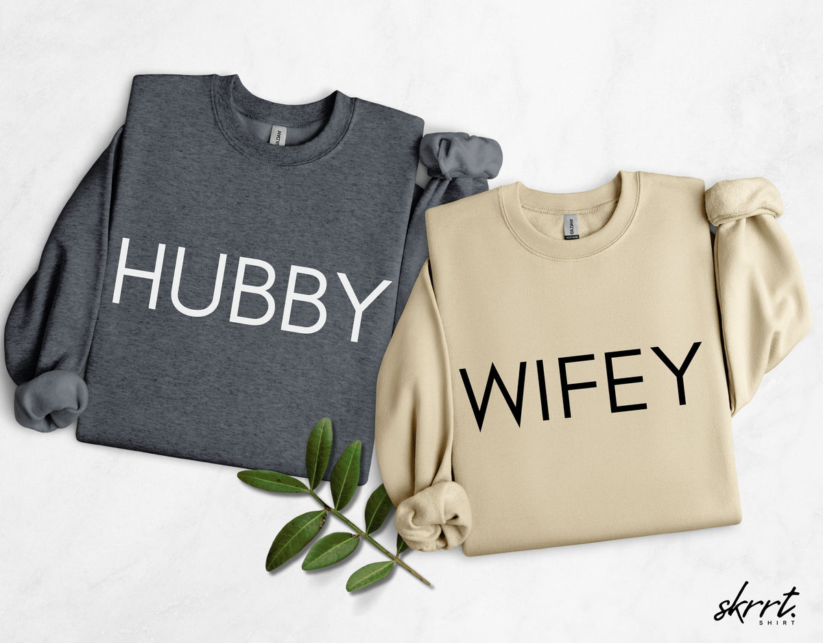 Koppel-sweaters: grijze “HUBBY” en beige “WIFEY”, beide met lange mouwen en borstopdruk