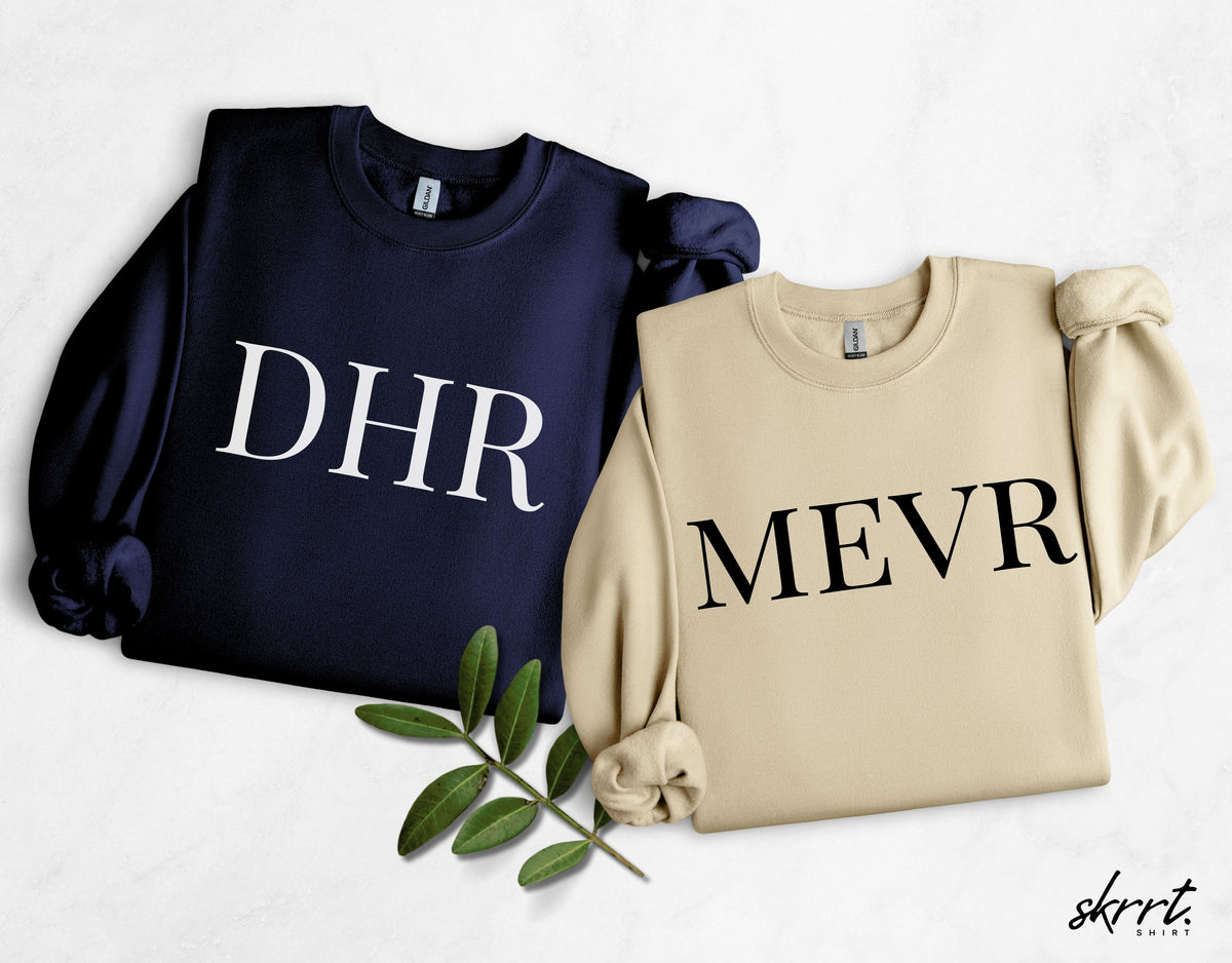 Twee sweatshirts: marineblauw met DHR en beige met MEVR, ronde hals, lange mouwen.